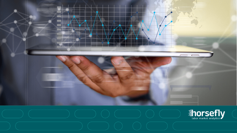 Image shows a hand holding a tablet flat with futuristic charts and stats emerging from the screen for the blog - Part 2: Leveraging External Labor Market Intelligence for Global Sourcing Success