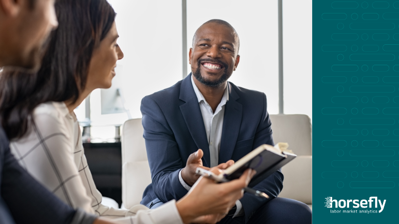 Image shows a smiling businessman working with members of his team, for the blog - Using Talent Acquisition Analytics Software to Optimize Hiring