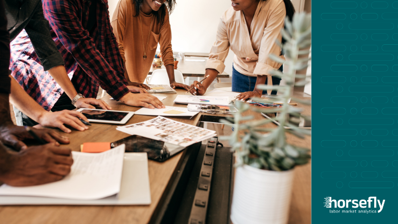 Image shows a group of people working around a table on a project, for the blog - Workforce Planning Analytics for Difficult-to-Hire Roles